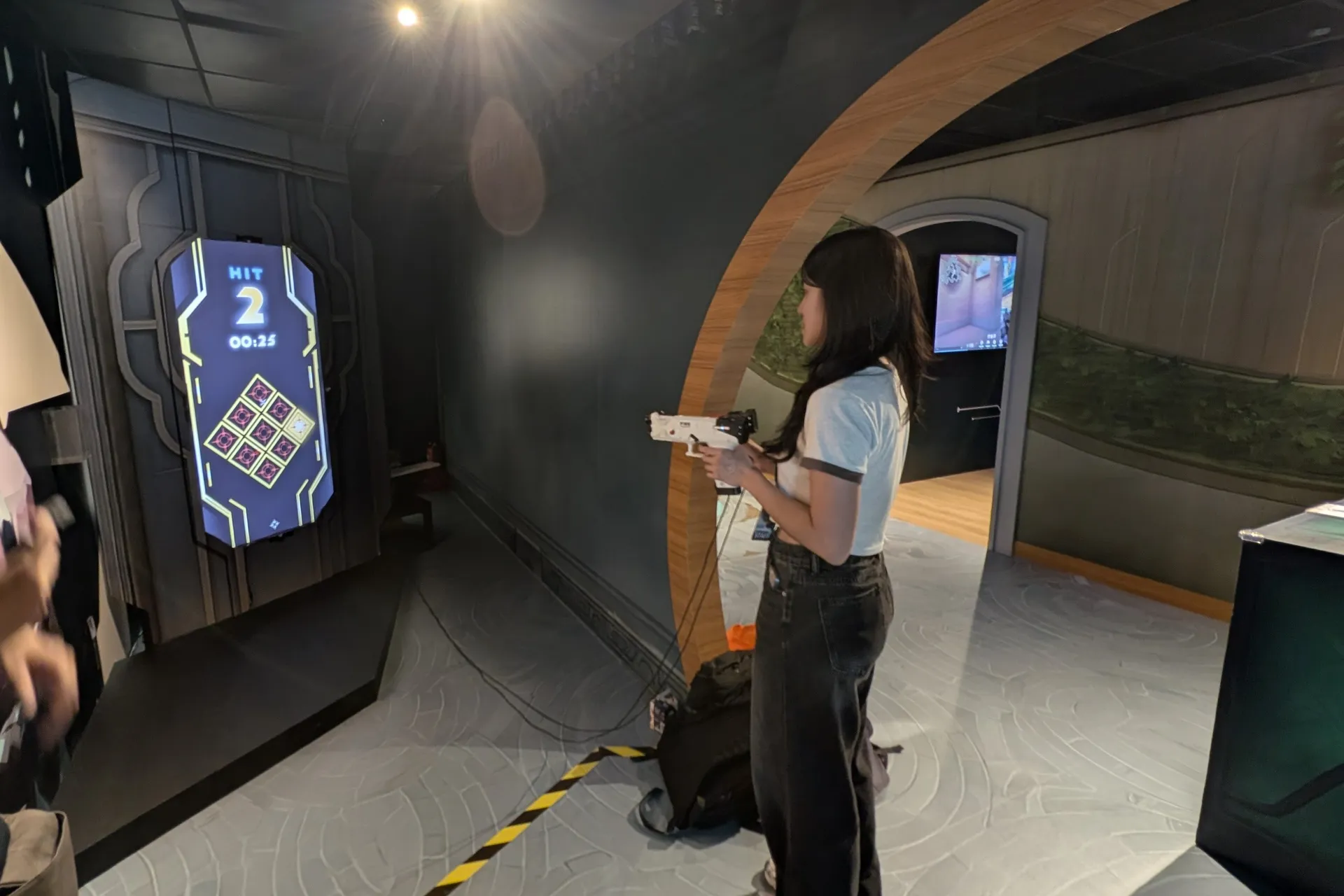 A visitor aims a light gun at the game screen set into the wall of the VALORANT themed exhibition