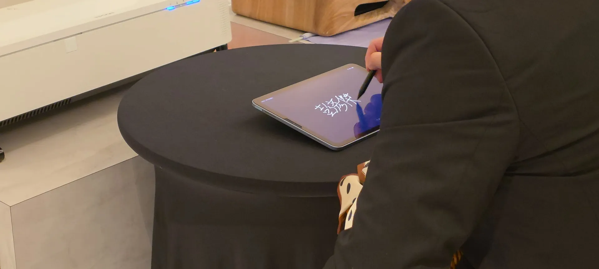 A guest signs on a tablet with a stylus; the projector sits behind the table