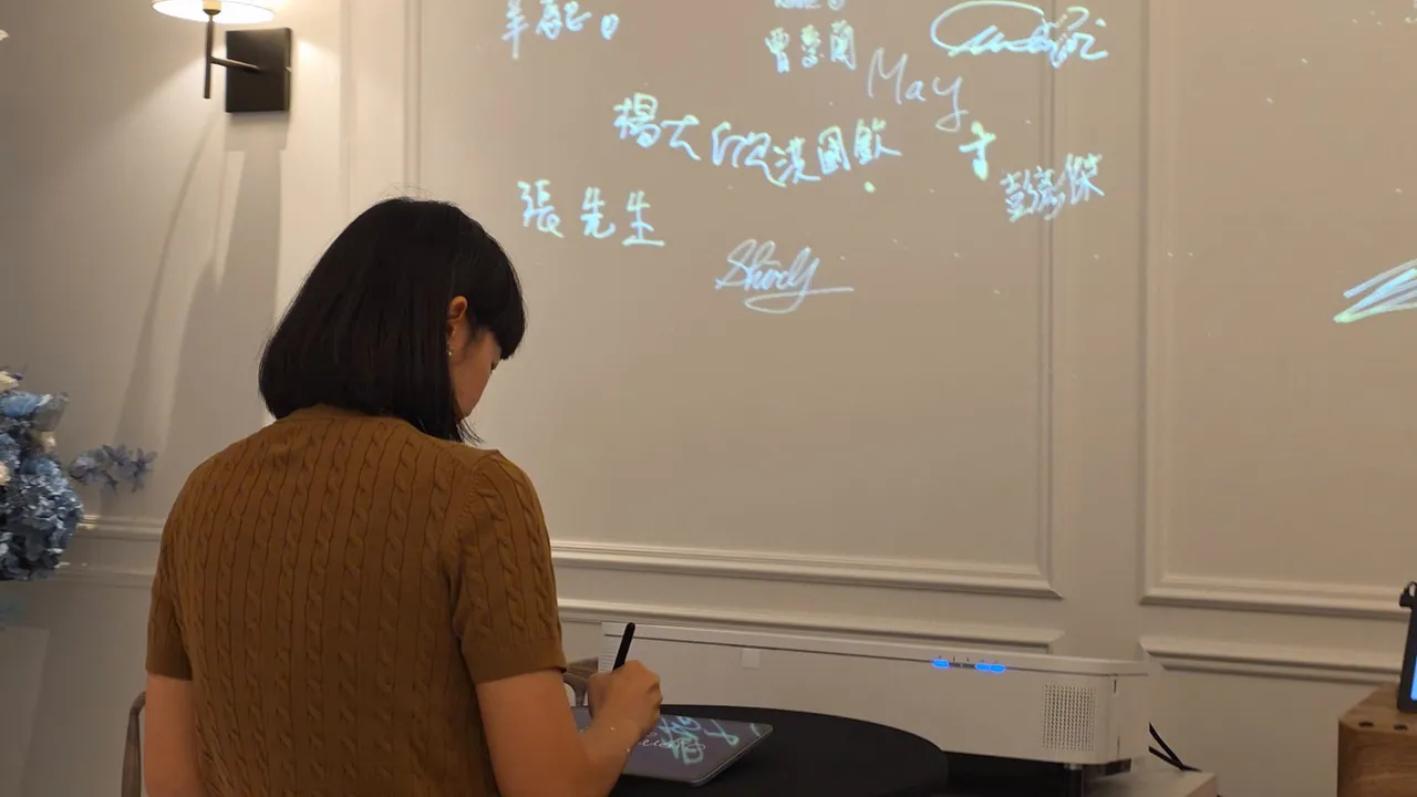 A guest, seen from behind, signs at the table with the signatures on the wall above her